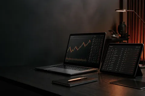 Modern trading workstation with a laptop and tablet showing market charts and an economic calendar